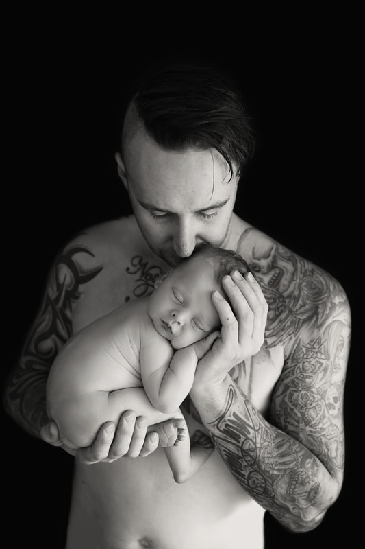 Tiny Feet Photography Black and White photo with Newborn baby posed with dad while he kisses his head