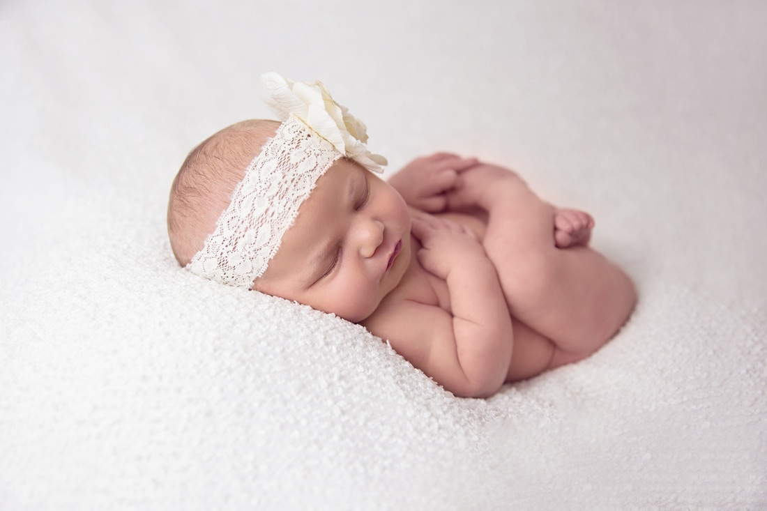 Tiny Feet Photography Newborn baby posing with headband on white blanket in huckfinn pose