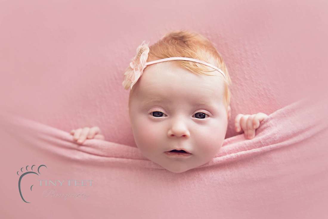Tiny Feet Photography Newborn baby girl posed on pink backdrop in tucked in