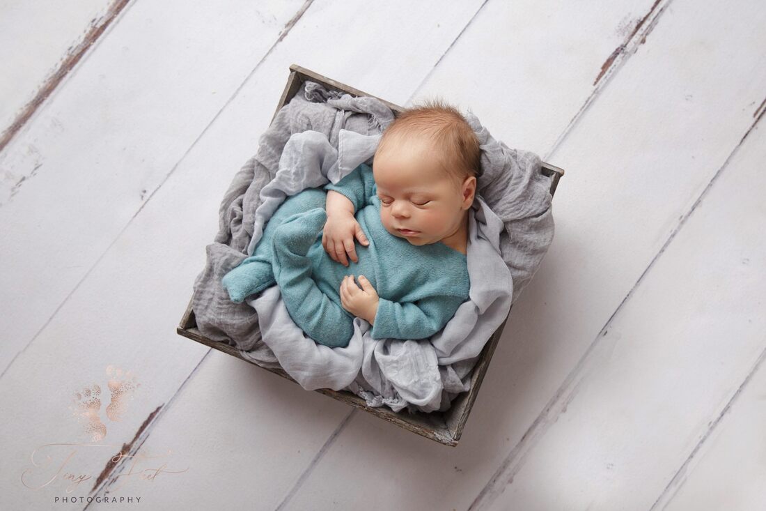 Tiny Feet Photography Newborn baby boy posed in grey box with grey fabric on white wood flooring 