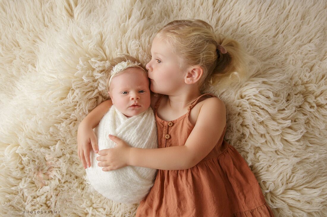 Tiny Feet Photography sibling pose with big sister cuddling newborn baby on flokati rug 