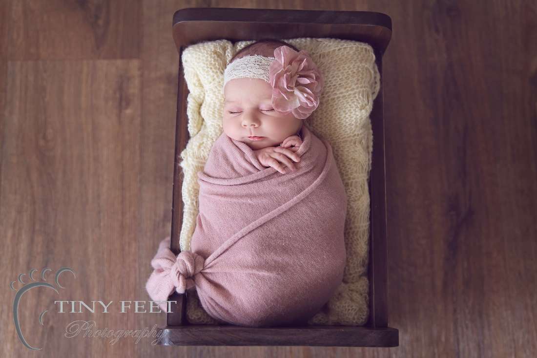 Tiny Feet Photography Newborn wrapped in pink wrap posed in wooden bed