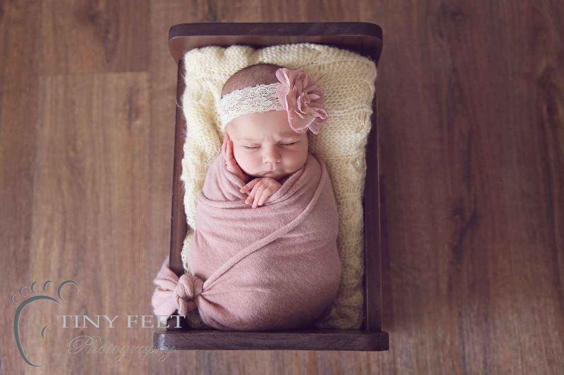 Tiny Feet Photography Newborn wrapped in pink wrap posed in wooden bed