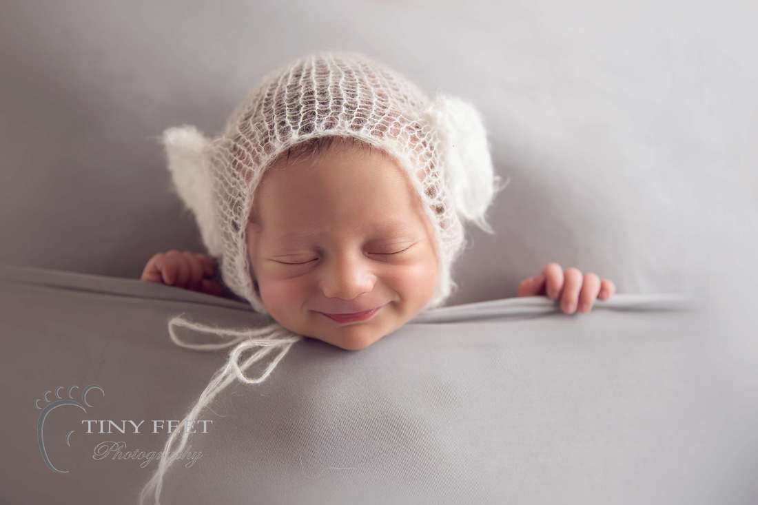 Tiny Feet Photography smiling baby in the tucked in pose on grey blanket