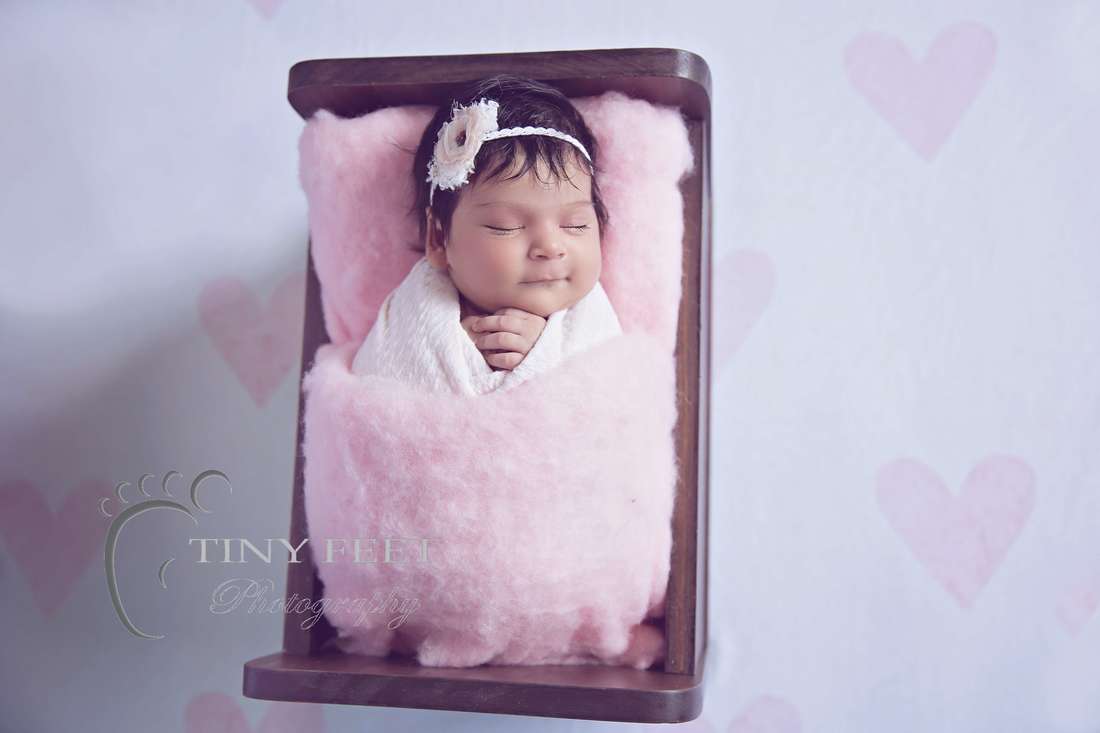 Tiny Feet Photography newborn baby girl posed in pink on a wooden bed