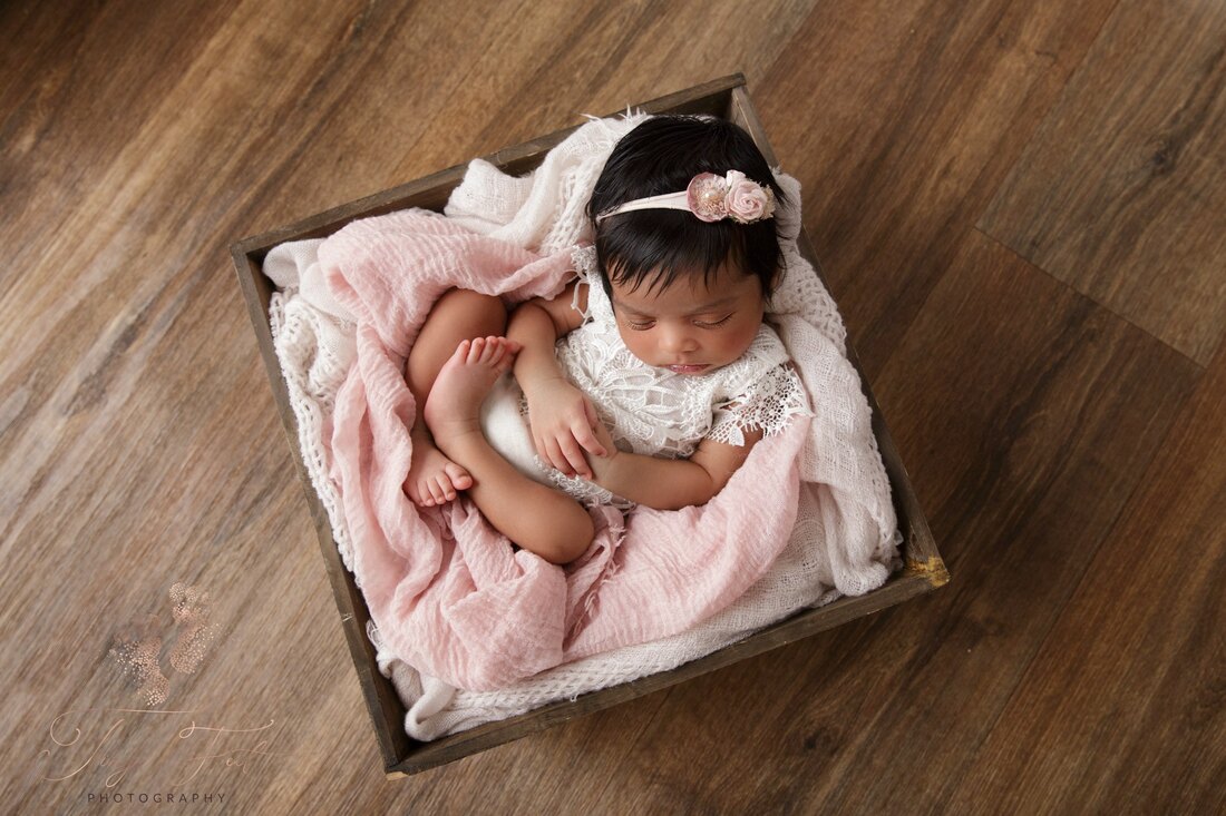Newborn girl in wooden box with pinks