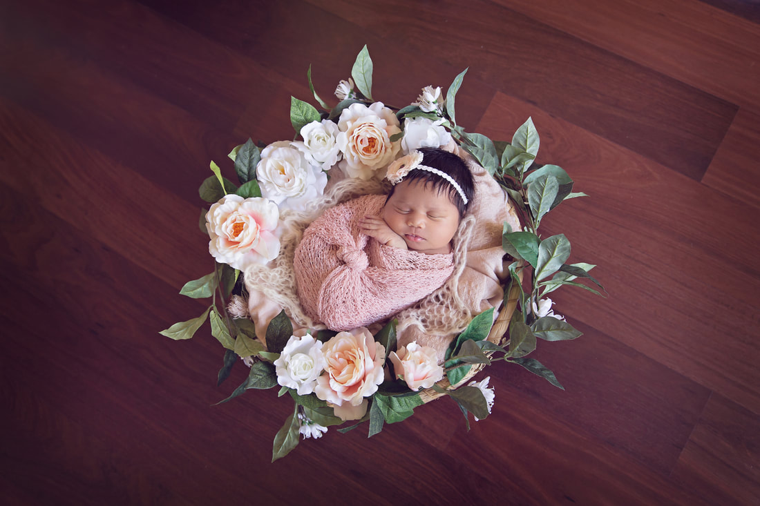 Newborn girl in pink with flowers in basket
