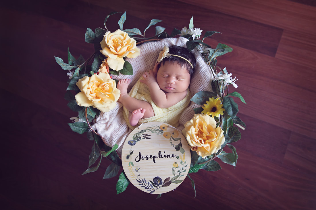 Newborn girl in yellow with flowers in basket