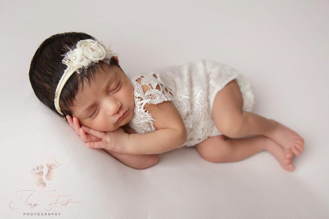 Tiny Feet Photography image of a sweet baby girl in Lacey white outfit in side pose on white fabric