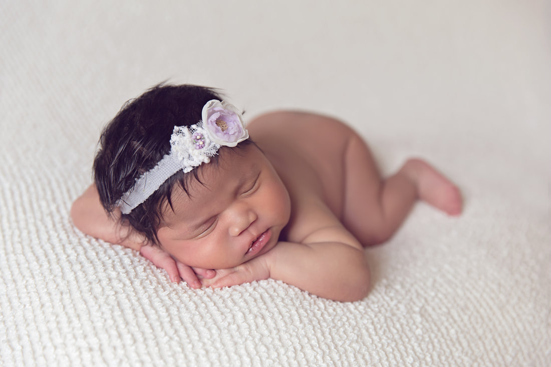Newborn baby girl chin on hands posing on cream blanket on beanbag
